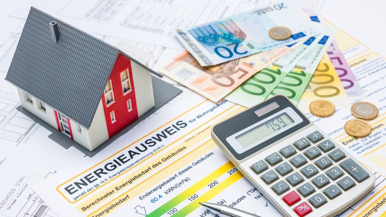 Modellaus, Taschenrechner, Geldscheine und -münzen liegend auf Bauplan